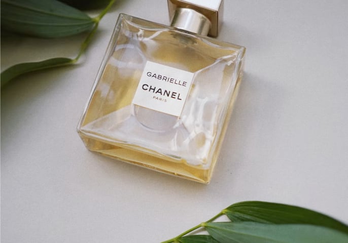 bottle of Gabrielle Essence Eau De Parfum lying on a table surrounded by leaves